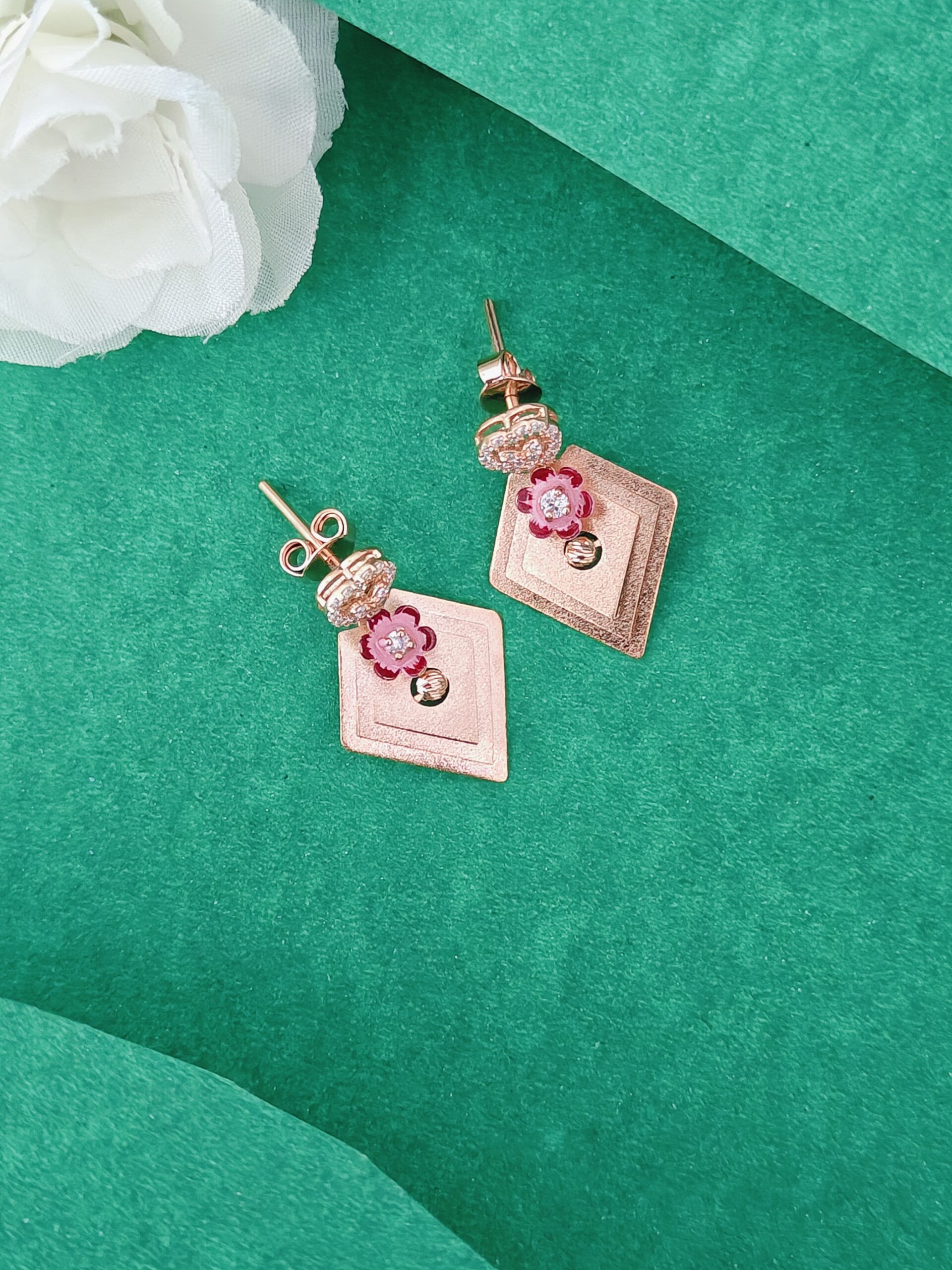 Rose gold earrings with floral designs on a green surface with a white flower.